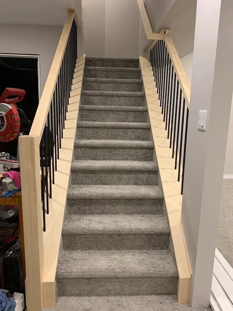 Basement stairs with a wood railing and black spindles on each side