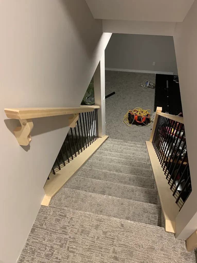 Basement stairs with a handrail on wall brackets and a railing with black spindles