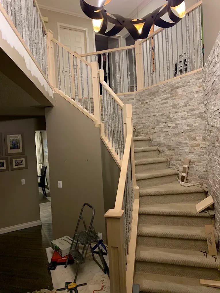 After: a new wood railing and metal spindles on the same faceted sweeping staircase, spindles still wrapped during the install
