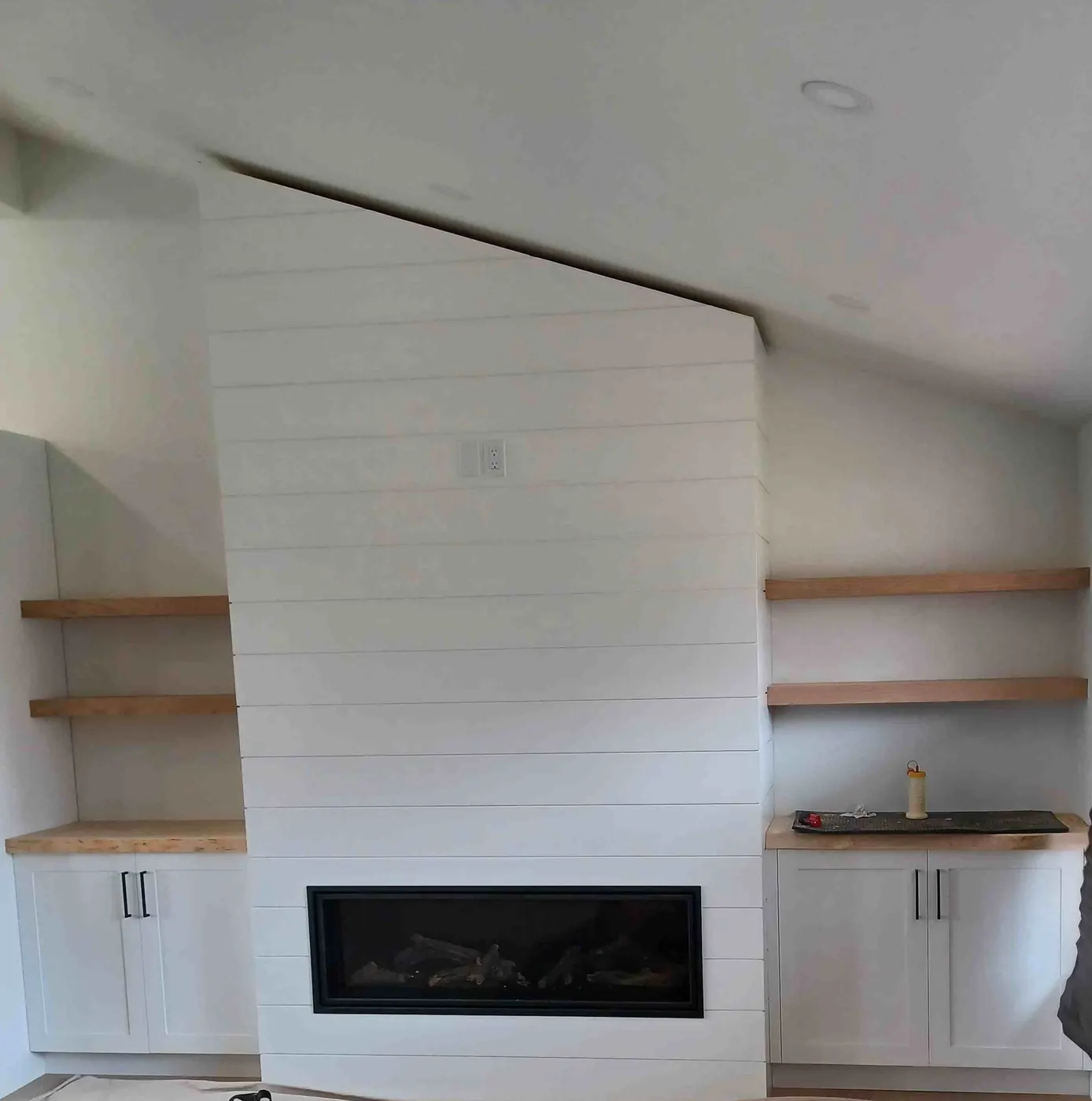 Shiplap fireplace wall with built-in cabinets and wood floating shelves on each side
