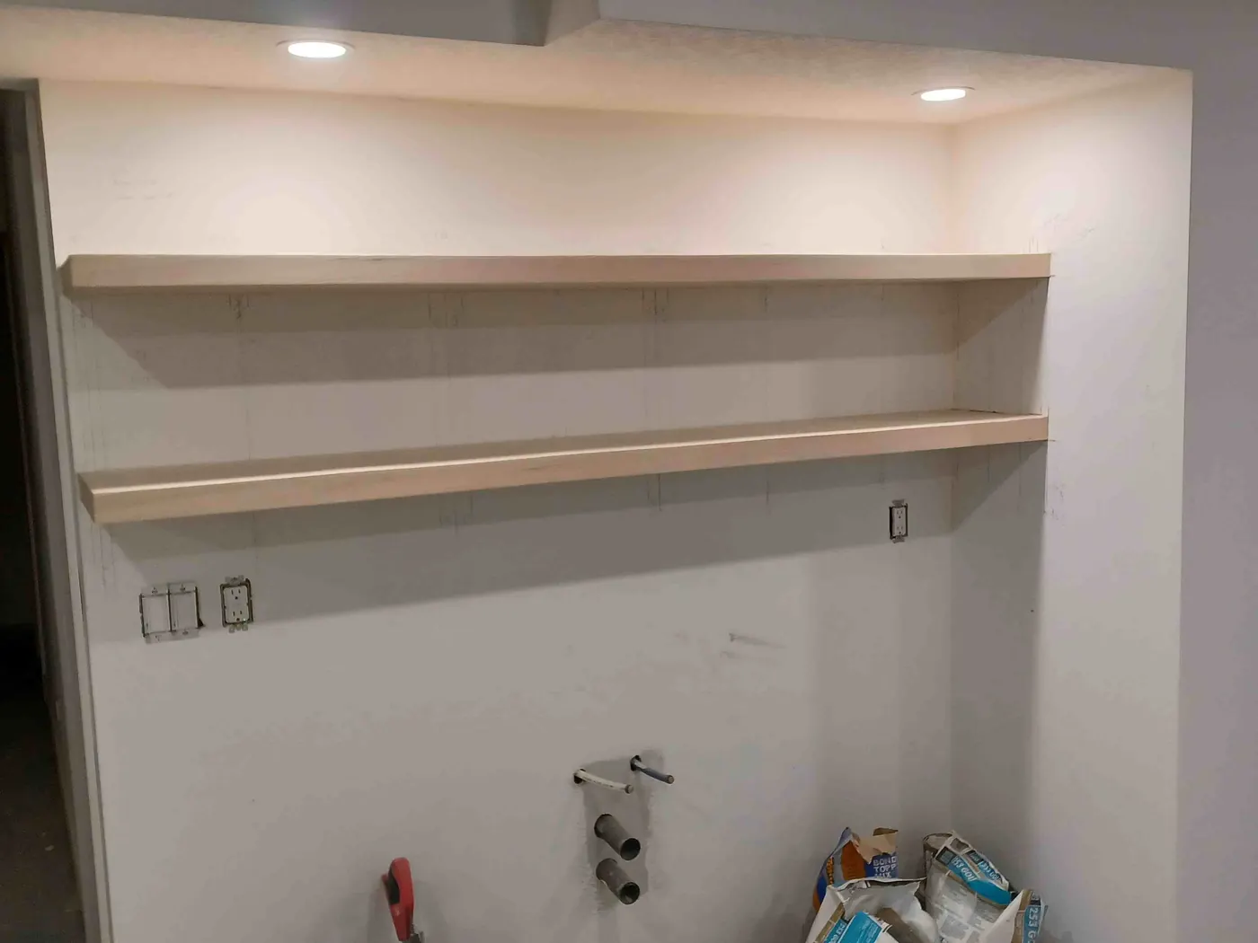 Two long wood floating shelves on a basement suite kitchen wall, before the counters go in