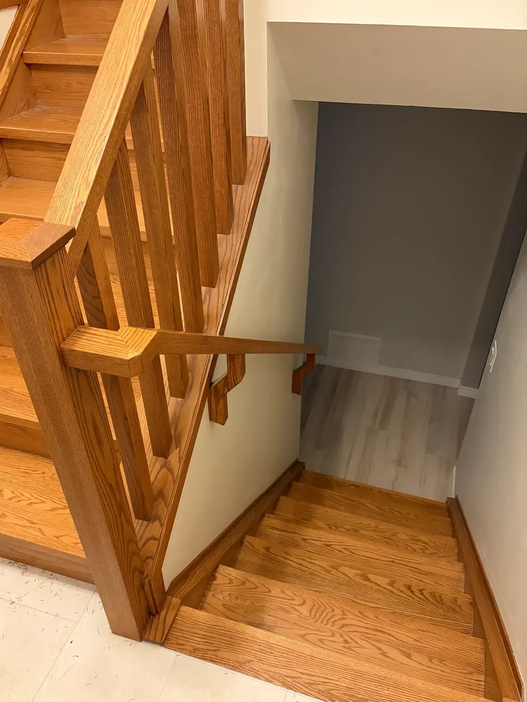After: new wood treads, an open railing with square spindles and a capped newel post where the half wall was, and a wall handrail on wood brackets down the lower flight