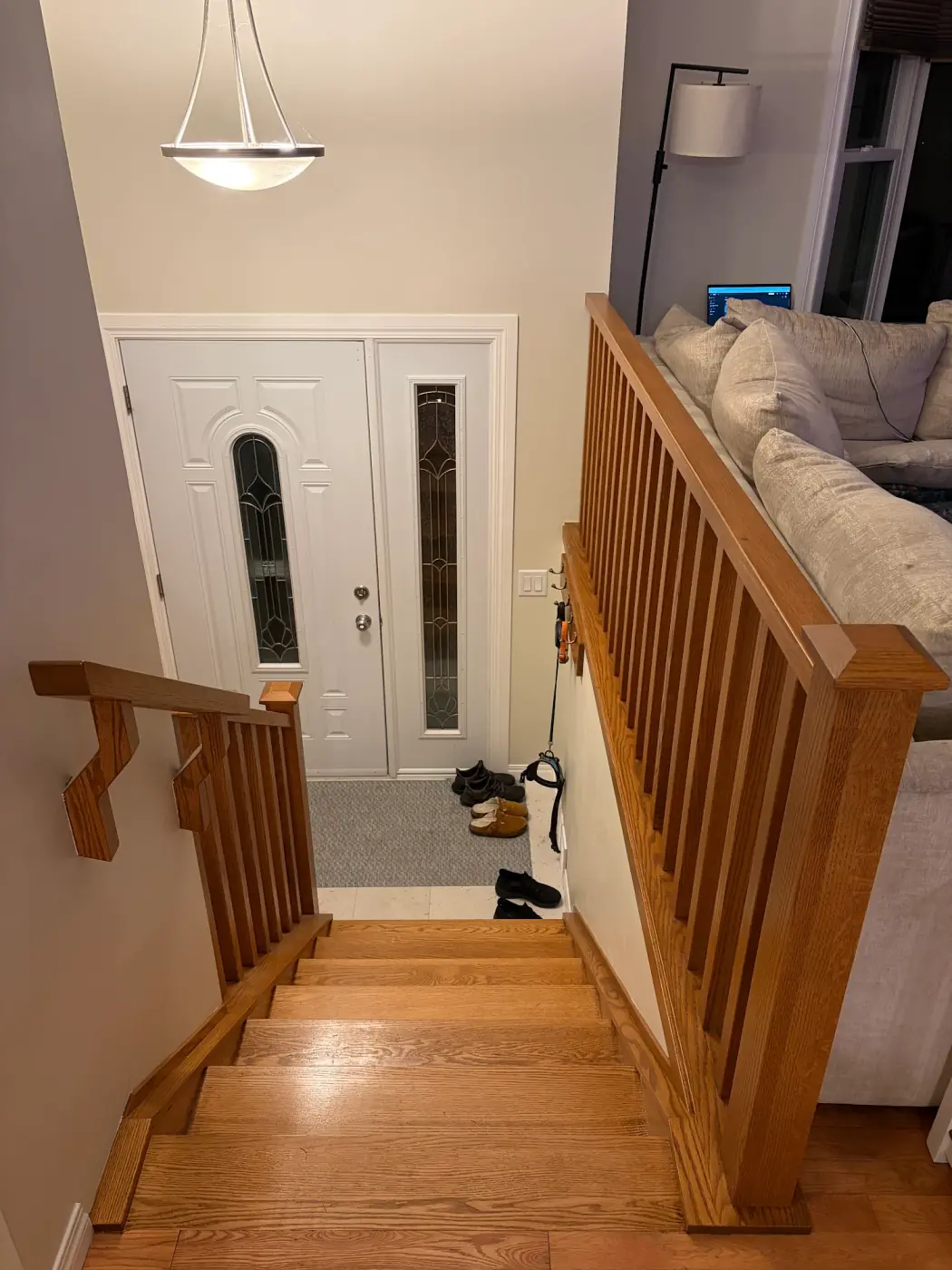 Wood railing with square spindles along an upper-floor living room, above stairs that lead down to the front door, with a wall handrail on wood brackets
