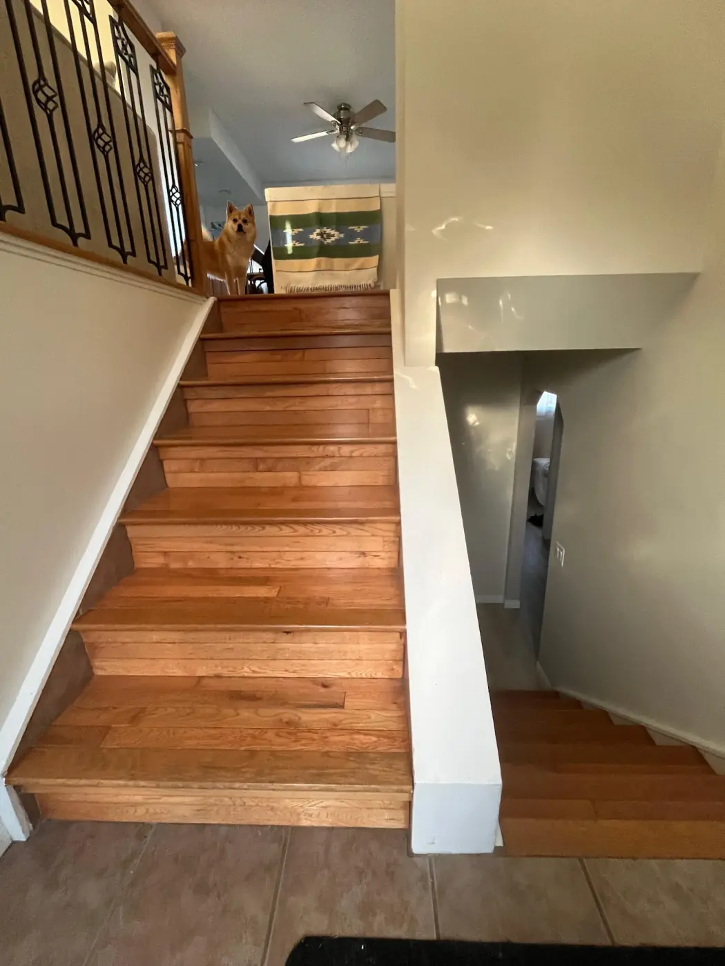 Before: stairs going up beside stairs going down, split by a solid white half wall, with no handrail on either flight