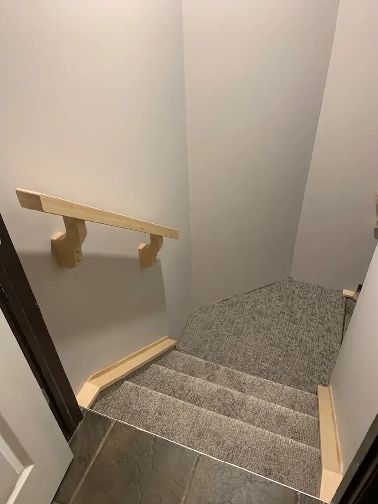 Unfinished wood handrail on wall brackets, with wood capping along both sides of a short carpeted stair