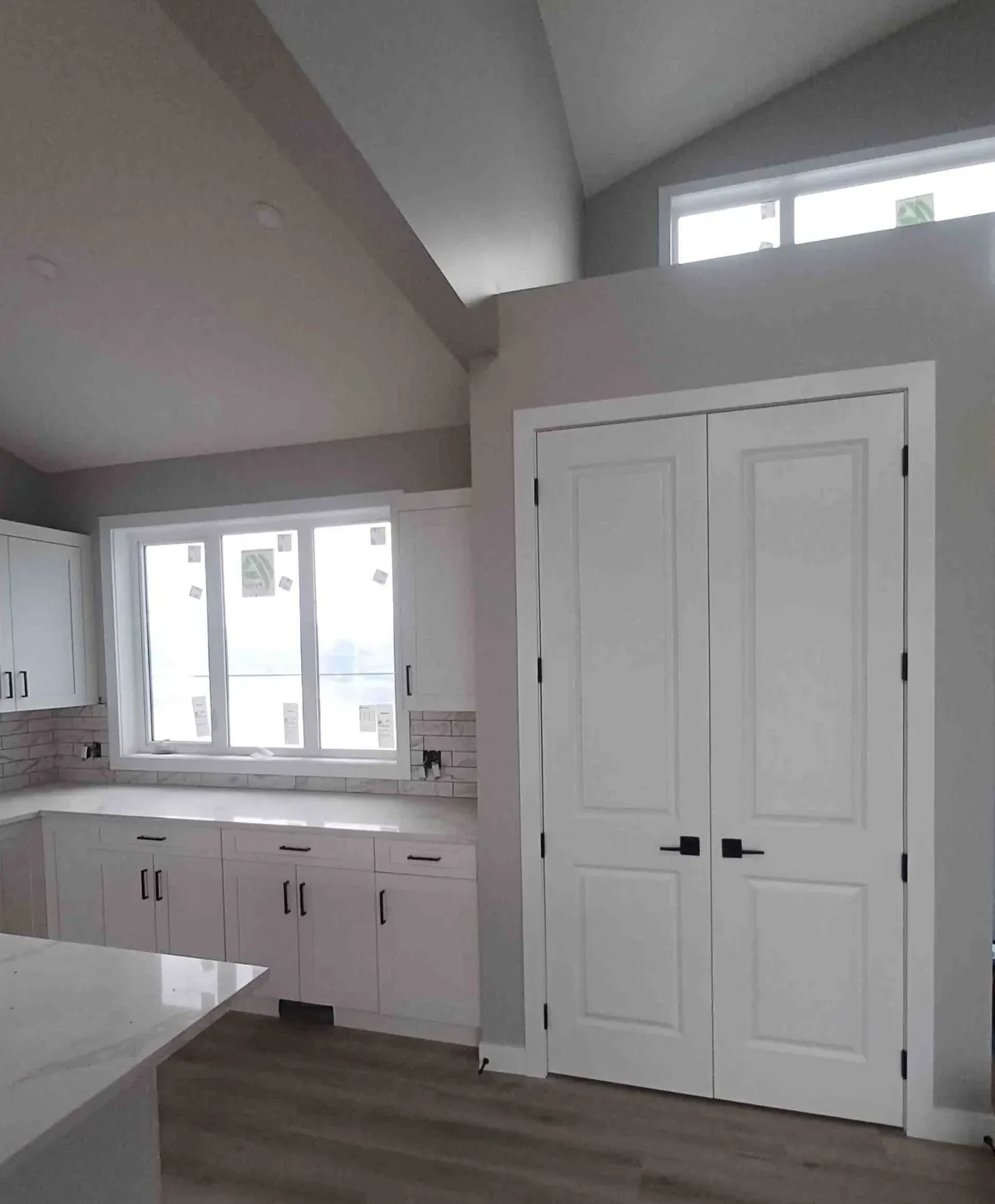 White double doors with casing beside a kitchen under a vaulted ceiling
