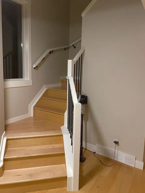 White newel post with black metal spindles and a wall handrail on light wood stairs
