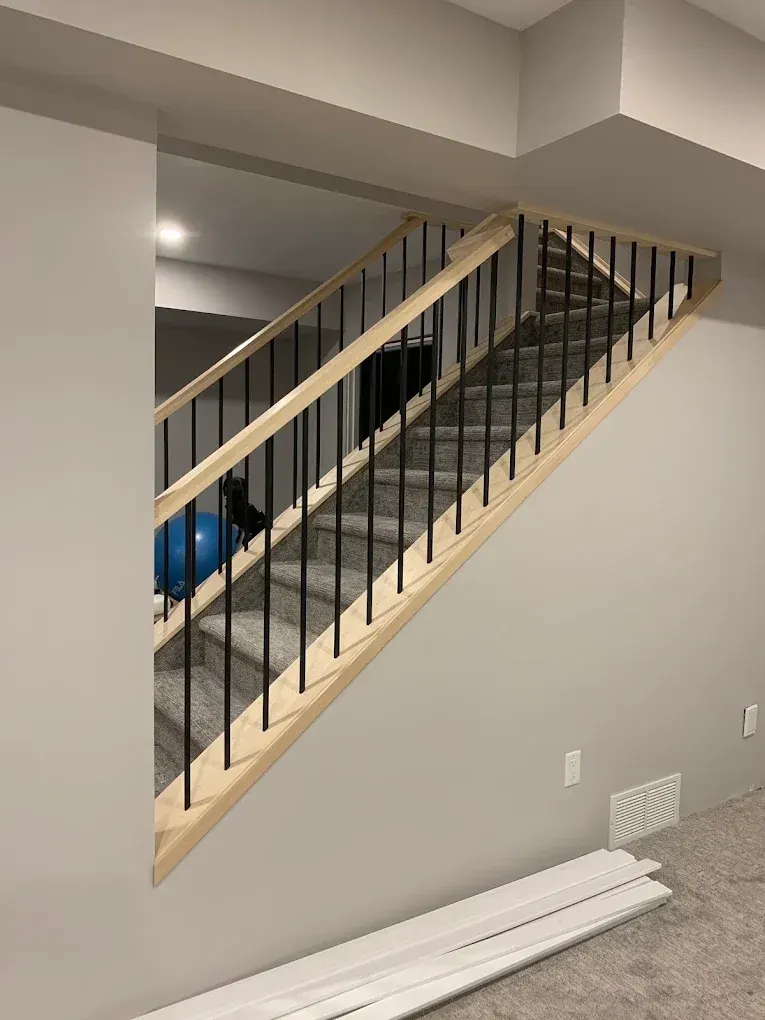 Maple handrail with a clear finish and black spindles above a basement stairwell half wall