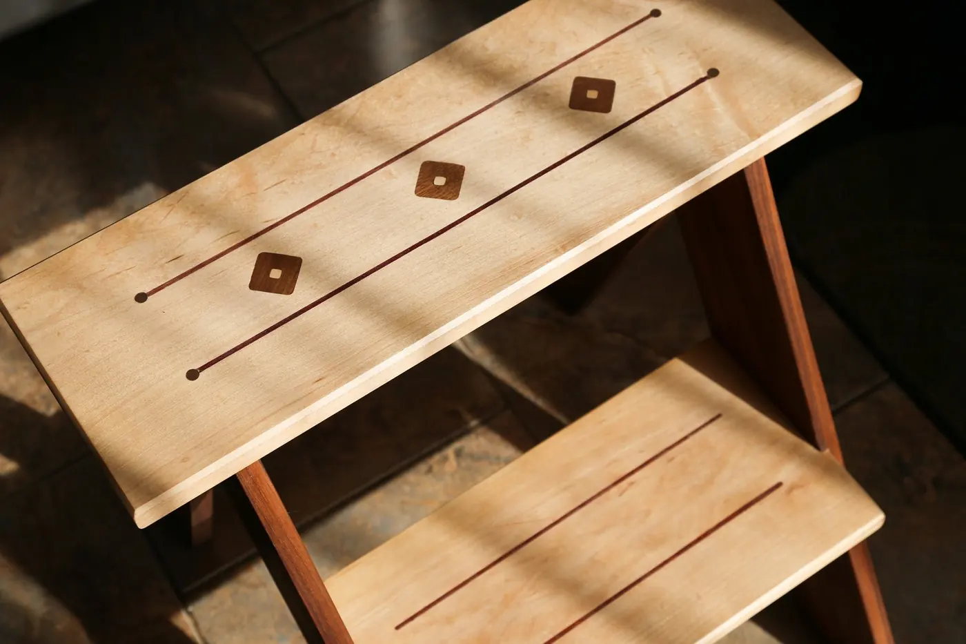Top of a wood step stool with inlaid dark wood lines and diamonds
