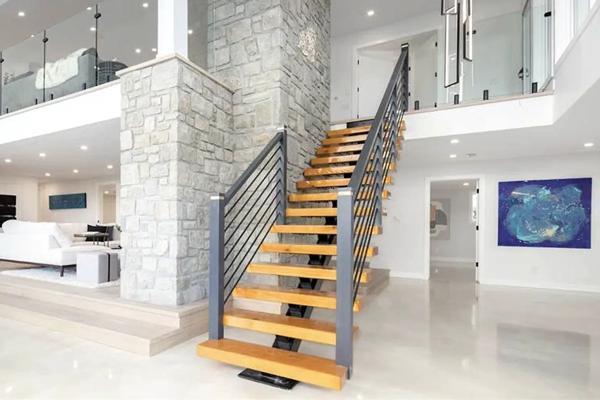 Open staircase with a horizontal metal railing beside a stone column